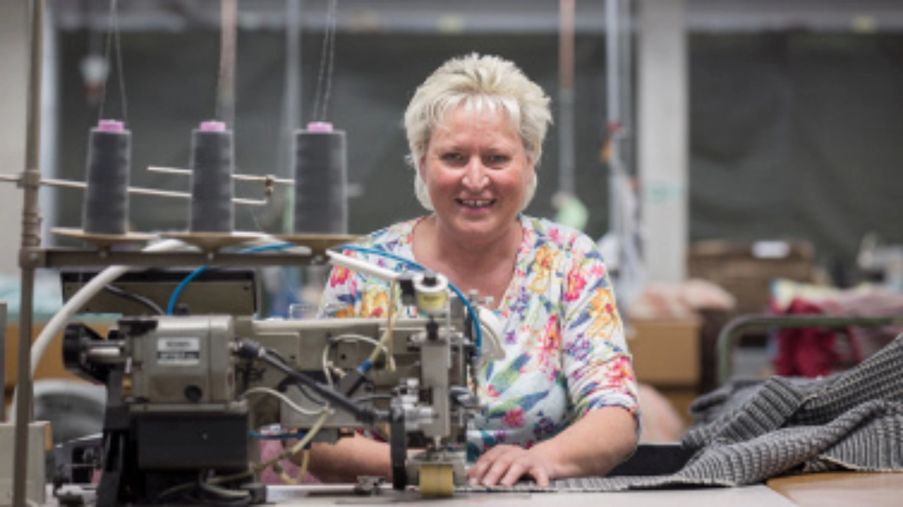Eine lachende Frau sitzt an einer Nähmaschine.