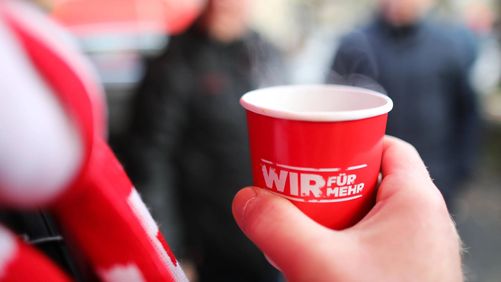 Jemand hält einen roten Becher mit dampfendem Kaffee.