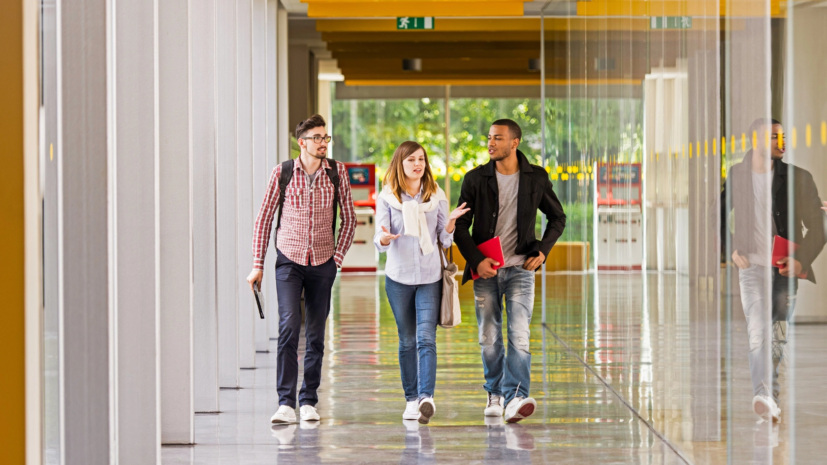 Eine Studentin und zwei Studenten laufen über einen Korridor und unterhalten sich dabei.