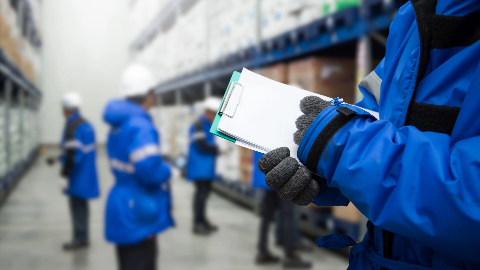 ein Beschäftiger prüft Lagerware in einem Kühlraum, im Hintergrund weitere Kolleginnen und Kollegen