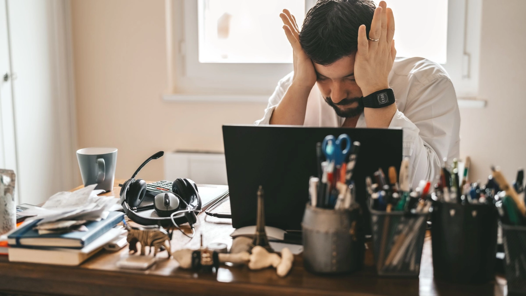 Beschäftigter im Homeoffice legt sich sichtbar gestresst die Hände vor die Stirn.