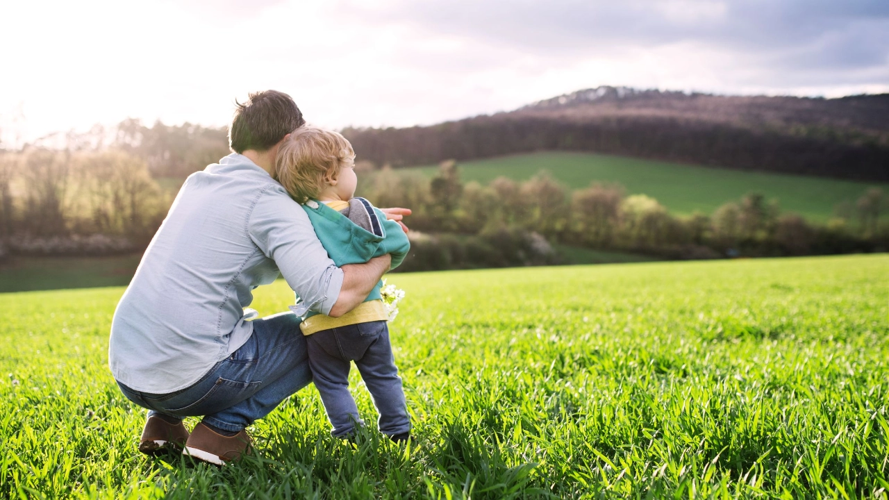 ein Vater schaut mit seinem Kind über eine grüne Landschaft